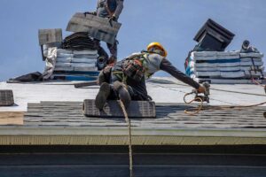Person with safety harness and rubber-soled shoes carefully walking on a sloped shingled roof.