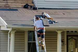 Roofing workers install shingles on a residential roof while examining underlayment and flashing.