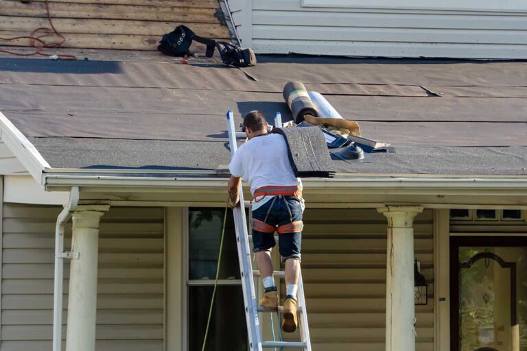Roofing workers install shingles on a residential roof while examining underlayment and flashing.