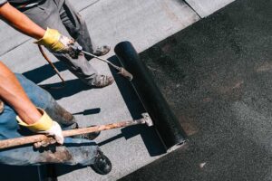 A homeowner checks roof shingles and clears leaves from a gutter before leaving for vacation.